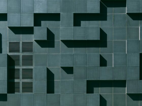 Teal tiled building facade with square panels and deep geometric shadows forming stair-step patterns.