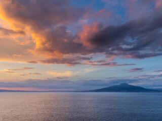 Sunset over calm sea with distant mountains and colorful orange, pink, and purple clouds in the sky
