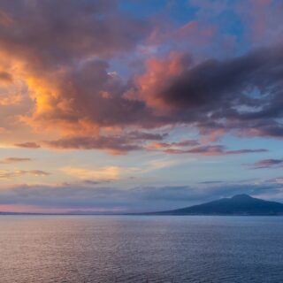 Sunset over calm sea with distant mountains and colorful orange, pink, and purple clouds in the sky