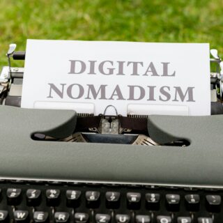 Vintage typewriter with a sheet reading 'DIGITAL NOMADISM' against a green lawn backdrop.