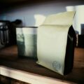 Beige kraft paper bag with a small skull stamp on the bottom corner, resting on a wooden shelf.