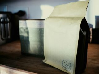 Beige kraft paper bag with a small skull stamp on the bottom corner, resting on a wooden shelf.