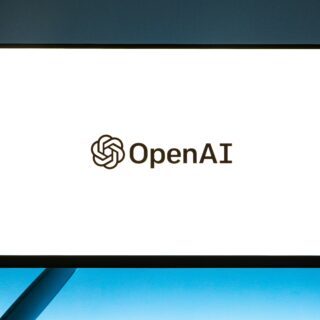 Monitor displaying the OpenAI logo on a bright white screen against a blue backdrop, logo centered low on the display.