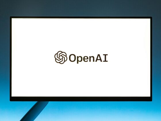 Monitor displaying the OpenAI logo on a bright white screen against a blue backdrop, logo centered low on the display.