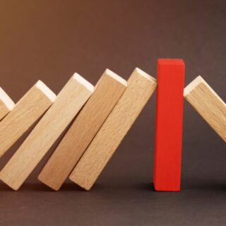 A red upright domino stops a line of falling wooden dominoes, breaking the chain reaction.