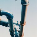 Blue industrial pipes with flanged joints and bolts stretching against a clear sky.