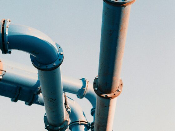 Blue industrial pipes with flanged joints and bolts stretching against a clear sky.