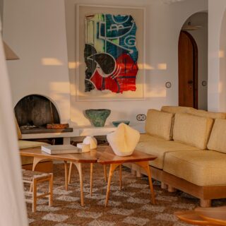 Cozy living room with a beige sectional, two round wood coffee tables, abstract painting over a fireplace, and a woven room divider.