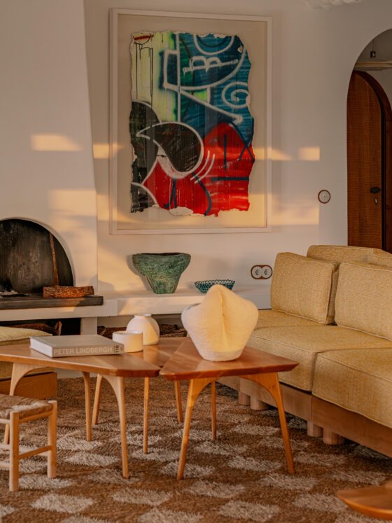 Cozy living room with a beige sectional, two round wood coffee tables, abstract painting over a fireplace, and a woven room divider.