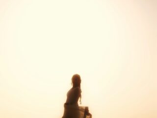 Silhouetted woman dancing on the beach at sunset, a flowing dress catching the breeze with a large sun behind.
