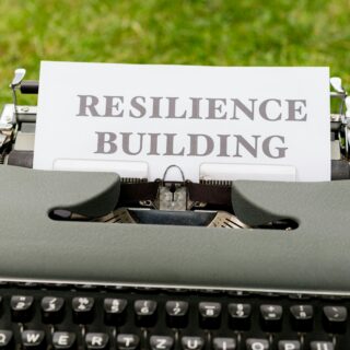 Vintage typewriter on a stone surface with a sheet reading RESILIENCE BUILDING, outdoors on grass.