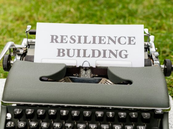 Vintage typewriter on a stone surface with a sheet reading RESILIENCE BUILDING, outdoors on grass.