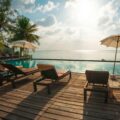 Resort deck with wooden loungers, umbrellas, and palm trees overlooking a calm ocean under a sunny sky.