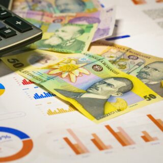 Calculator atop scattered banknotes and financial charts on a desk, suggesting budgeting or accounting activity.