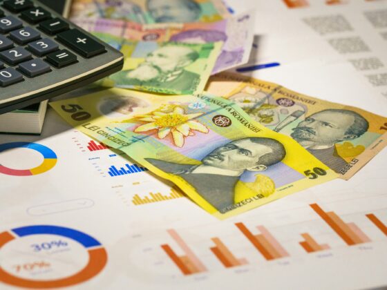 Calculator atop scattered banknotes and financial charts on a desk, suggesting budgeting or accounting activity.