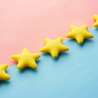 Yellow star-shaped objects lined diagonally on a pastel pink and blue background, creating a playful decorative scene.