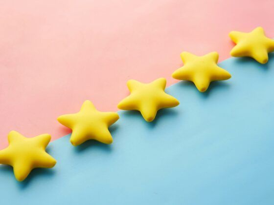 Yellow star-shaped objects lined diagonally on a pastel pink and blue background, creating a playful decorative scene.