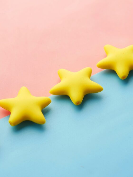 Yellow star-shaped objects lined diagonally on a pastel pink and blue background, creating a playful decorative scene.