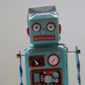 Blue tin toy robot facing the camera with red cheeks, round eyes, and gauges on its chest area.