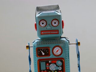 Blue tin toy robot facing the camera with red cheeks, round eyes, and gauges on its chest area.