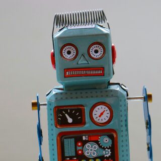 Blue tin toy robot facing the camera with red cheeks, round eyes, and gauges on its chest area.