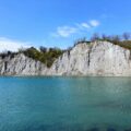 Blue lake with a rocky cliff and sparse trees along the shore under a clear sky, spring landscape.