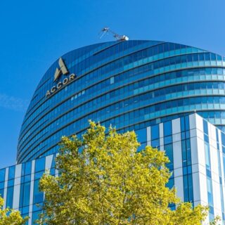Curved glass-fronted office building with the Accor logo, under a clear blue sky, with trees in the foreground.