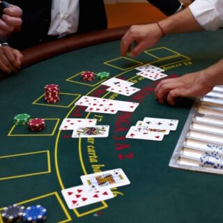 Blackjack table with players’ cards dealt, hands resting near the felt and a rack of colored poker chips on the right.