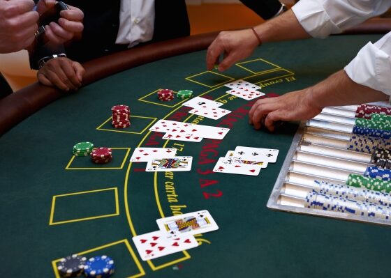 Blackjack table with players’ cards dealt, hands resting near the felt and a rack of colored poker chips on the right.