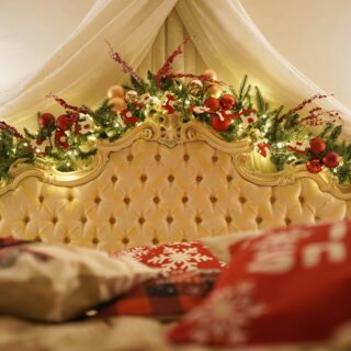 Festive Christmas garland and ornaments arranged along an ornate tufted bed headboard under a white canopy.