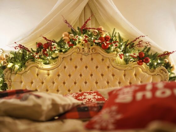 Festive Christmas garland and ornaments arranged along an ornate tufted bed headboard under a white canopy.