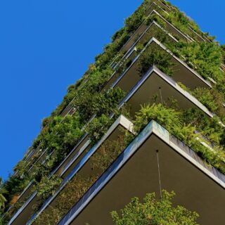 Tall residential building with cascading greenery on every balcony against a blue sky.