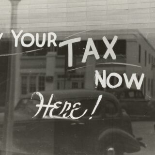 Sign on a window reading 'PAY YOUR TAX NOW' urging viewers to pay taxes now.