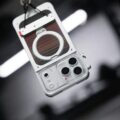 Close-up of a vintage-style camera with a round lens housing and carbon-fiber panel, hanging from a strap.