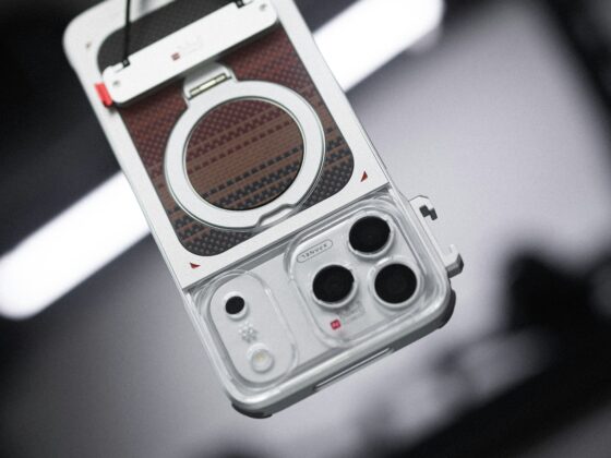 Close-up of a vintage-style camera with a round lens housing and carbon-fiber panel, hanging from a strap.