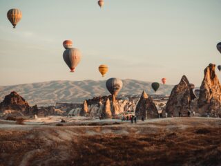 Colorful hot air balloons drifting above rugged rock formations at sunrise in Cappadocia, Turkey.