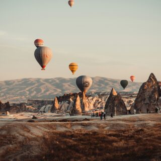 Colorful hot air balloons drifting above rugged rock formations at sunrise in Cappadocia, Turkey.