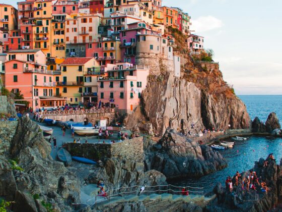 Colorful houses stacked on a cliffside village overlooking the sea, with boats along the rocky shore below.