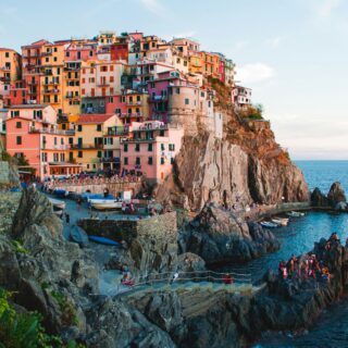 Colorful hillside houses stacked on a cliff above a rocky shore with boats in the water.