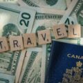 Canadian passport resting on scattered U.S. dollars with wooden Scrabble tiles spelling TRAVEL, conveying travel finance imagery.