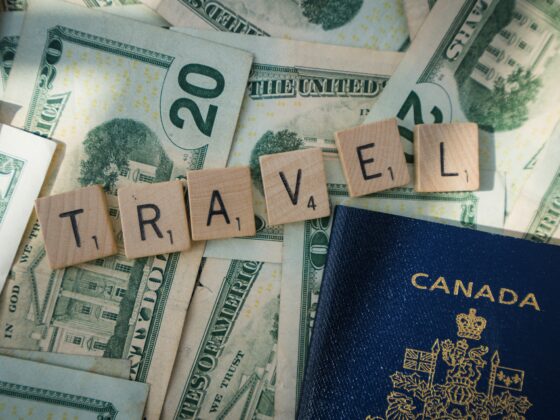 Canadian passport resting on scattered U.S. dollars with wooden Scrabble tiles spelling TRAVEL, conveying travel finance imagery.