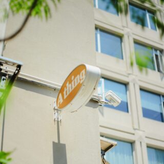 Orange circular sign reading 'Chips' mounted on a beige building with large glass windows and green foliage in the foreground.