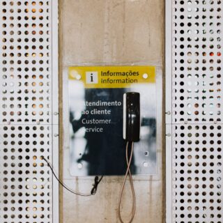 Public information area with a yellow bilingual sign reading 'Informações/Information' and a payphone, framed by perforated metal panels.