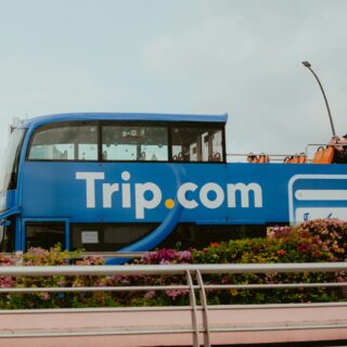 Blue double-decker tour bus with Trip.com branding, passengers on the open top deck taking photos under a cloudy sky.