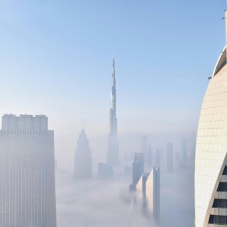 City skyline with fog, featuring a tall central skyscraper and a large angular building on the right.