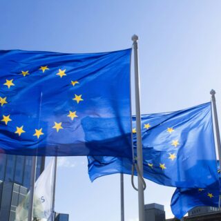 European Union flags fluttering on flagpoles against a blue sky in an urban setting