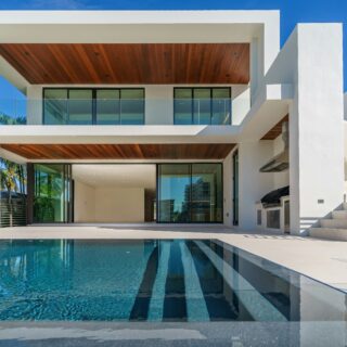 Modern white, two-story house with glass balcony and a blue reflecting pool in front under a clear sky.