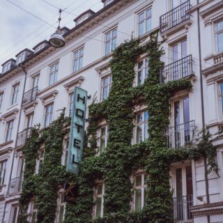 White building facade with ivy climbing the walls and a vertical 'HOTEL' sign.