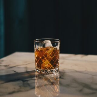 Whiskey on a cut-glass tumbler with ice, set on a marble counter with a dark moody background.