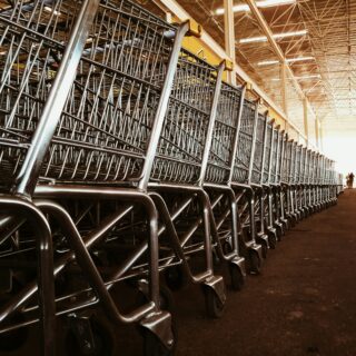 Row of metal shopping carts lined up along an aisle in a large warehouse.